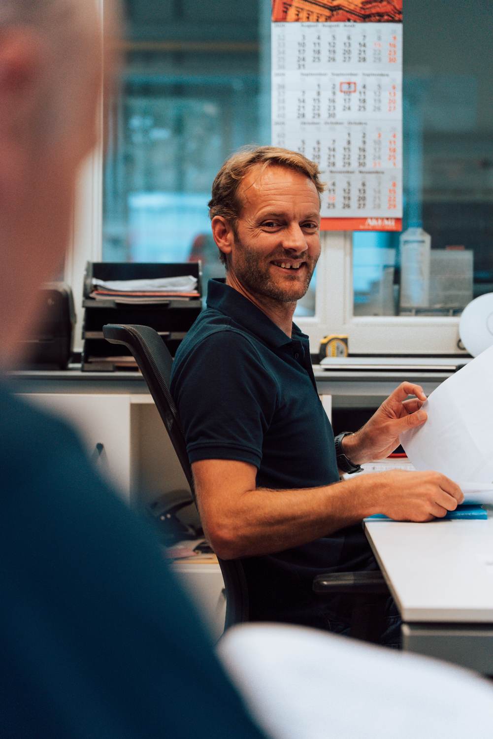Werkvoorbereider lachend aan zijn bureau